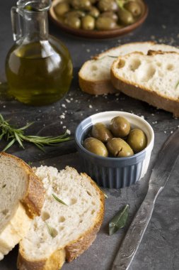 İtalyan dilimlenmiş ciabatta ekmeği otlarla doğranmış, ekstra bakire yağı ve koyu grunge arka planda marine edilmiş zeytinler.