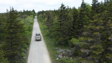 Bir gözyaşı karavanıyla açık havadaki aile manzarası, yeşil ağaçlar ve kırsal kesimde doğa ile çevrili manzaralı toprak bir yolda seyahat etmek..