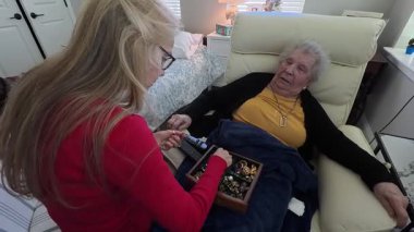 Yaşlı bir kadın ve kızı, bir huzurevi ziyareti sırasında mücevher kutusundan baktıklarında samimi bir anı paylaşıyorlar..