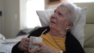 Yaşlı bir kadın, bir ev sağlık merkezinde rahat bir şekilde oturup sıcak bir içki yudumluyor ve huzur içinde çevresinin tadını çıkarıyor..