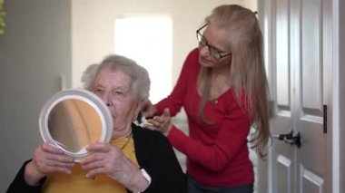 Sağlık merkezindeki yaşlı bir kadın, kişisel bakım sırasında aynada kendisine bakarken bakım ve ilgi görüyor..