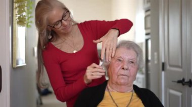 Bir bakıcı, bakım evinde yaşlı bir kadının saçını şekillendirir. Yardımsever yaşam için nezaket ve günlük destek gösterir..