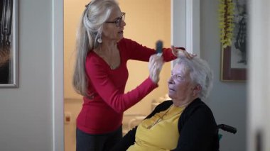 Bakıcı, evde yaşlı kadınların saçlarını nazikçe tarar. Sağlık merkezinde, sıcak bir ortamda bakım ve iletişimi teşvik eder..