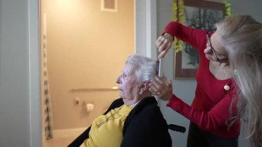 Bakıcı, huzur ve bakım tesisinde sakin ve sıcak bir ortamda yaşlı bir kadının saçını tarar..