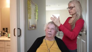 Yaşlı bir kadına, rahat bir sağlık hizmetinde, saçlarını tarayan bakıcı tarafından bakılıyor..