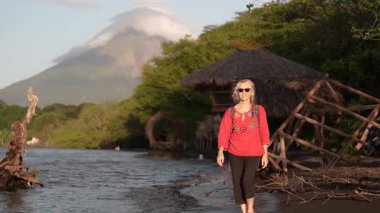 Olgun bir kadın Ometepe Adası kıyılarında yürürken, Madeira Volkanı ve berrak göl suyunu görür..