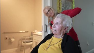 Yaşlı bir kadın, bakıcısı rahat bir sağlık merkezinde saçını şekillendirirken kişisel bakımdan zevk alıyor..
