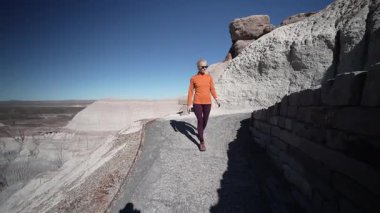 Olgun bir kadın, Arizona 'daki Petrified Forest Ulusal Parkı' nın manzarasını araştırmak için Mavi Mesa bölgesinde bir patika boyunca yürüyor.