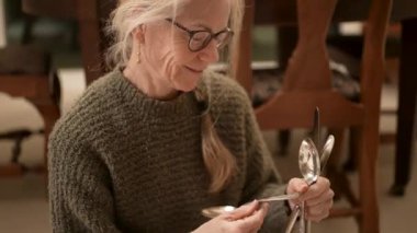 Olgun bir kadın, aile yadigarı gümüş çatal bıçak takımlarını dikkatlice dizer ve her parçanın ardındaki tarihi takdir eder..