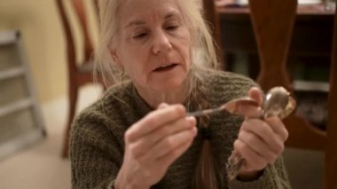Olgun bir kadın, ailesine miras kalan antika gümüş çatal bıçakları sınıflandırıyor. Her parçayı dikkatle inceler..