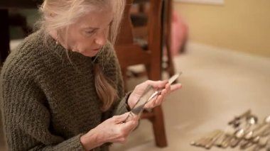 Olgun kadın, evinde ailesinden geçen gümüş çatal bıçakları dikkatlice inceler ve sınıflandırır..