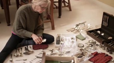 Olgun bir kadın, gün içinde oturma odasında gümüş çatal bıçak ve aile yadigarlarını dikkatlice sınıflandırır..