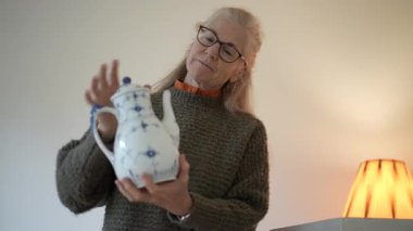 Olgun kadın aile antikalarıyla dolu kutuları açıyor ve oturma odasındaki her bir porseleni inceliyor..