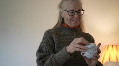 Olgun kadın, içinde aile antikaları ve aile yadigarlarının bulunduğu kutuları dikkatlice açarken gülümsüyor..