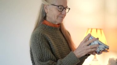 Olgun bir kadın, aile yadigârlarının ve antikalarının olduğu kutuları açar, her bir parçayı dikkatle ve dikkatle, oturma odasında inceler..