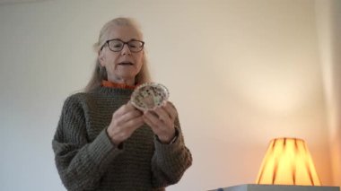 Aile yadigârına bakan olgun bir kadının portresi. Evinde anılarını ve hikayelerini sıcak tutuyor.