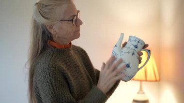 Olgun kadın aile yadigârlarıyla dolu kutuları açar. Evindeki her bir antikayı dikkatlice inceler ve tartışır..