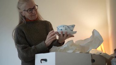 Olgun bir kadın aile antikaları ve aile yadigârlarıyla dolu kutuları açarken aile geçmişi ve anılarını yad eder..