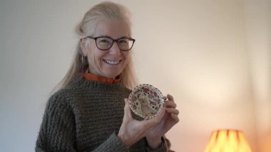 Aile yadigârına bakan olgun bir kadının portresi. Evinde anılarını ve hikayelerini sıcak tutuyor.