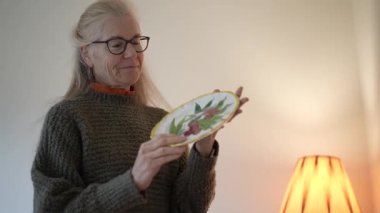 Olgun kadın, aile antikalarıyla dolu kutuları açar ve sıcak, davetkar mekanındaki her şeyi dikkatle inceler..