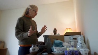 Olgun kadın kalıtsal eşyaları ve aile antikalarını inceler, sıcak bir odada sevdiklerinin anılarını yansıtır..