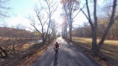 Batı Virginia 'da bir nehrin kenarındaki dolambaçlı bir yolda bisiklet süren bir kadın. Bu güzel günde sonbahar yaprakları onu sarıyor..