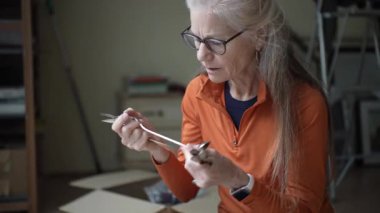 Olgun kadın, sıcak evindeki aile geçmişine ait anıları barındıran gümüş çatal bıçaklara yakından bakar.