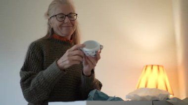 Olgun bir kadın, bir öğleden sonra evinde sıcak oturma odasında aile antikalarını ve aile yadigarlarını keşfedip açıyor..