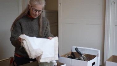 Olgun bir kadın, evindeki eski eşyaları ve aile yadigarlarını dikkatle taşır..