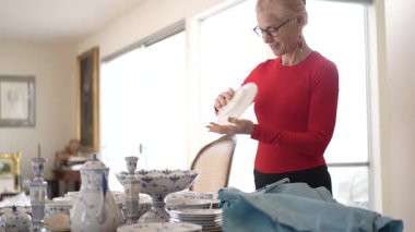 Olgun kadın antika porselenleri açıyor ve yemeklerden ve her bir parçanın arkasındaki geçmişi paylaşan aile anlarını yansıtıyor..