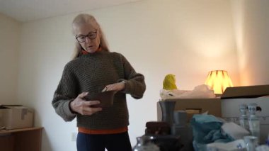 Olgun bir kadın, evindeki yurtdışı seyahatlerinden hatıralarla dolu bir kutu dolusu aile yadigarını karıştırıyor..