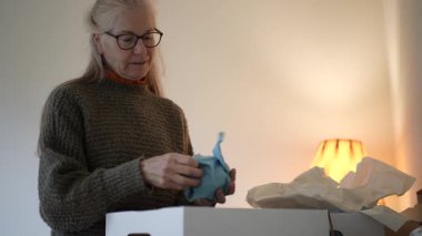 Olgun bir kadın, sıcak oturma odasında aile anılarını yansıtırken kutulardan antika yadigarları dikkatlice açıyor..