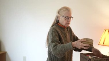 Olgun bir kadın evinde aile yadigârlarıyla dolu kutuları açarken anılarını ve tarihini araştırıyor..