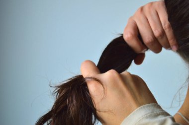 Ellerin yakın plan toplanması ve uzun siyah saçları at kuyruğu haline getirilmesi, temiz ve minimal bir arka plan ile günlük basit bir tımar rutini yakalaması..