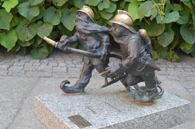 Bu ünlü bronz cüce heykeller Wroclaw, Polonya 'daki itfaiyecileri resmediyor. Gri granit bir tabanda, canlı yeşil yapraklardan oluşan bir duvara karşı konumlandırılmışlardır. Bu rakamlar, kentin kültürel mirasının popüler bir turizm merkezi ve simgesi..