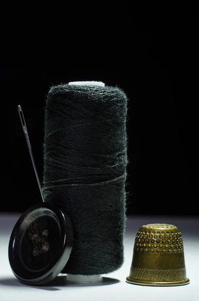 Carretel de fio preto com um dedal de agulha e um botão — Fotografia de Stock
