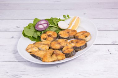 Kızarmış balık, limon ve soğanlı deniz yemeği tabağı.