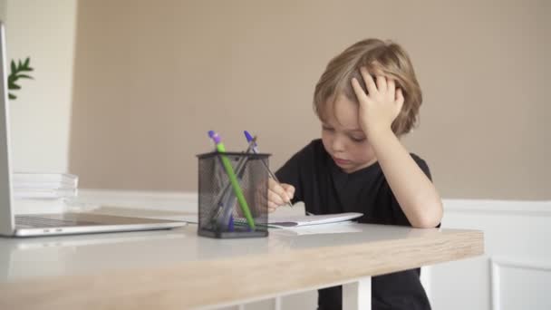 Een kind doet huiswerk met een laptop terwijl hij thuis in de keuken aan tafel zit. Online-technologie. — Stockvideo