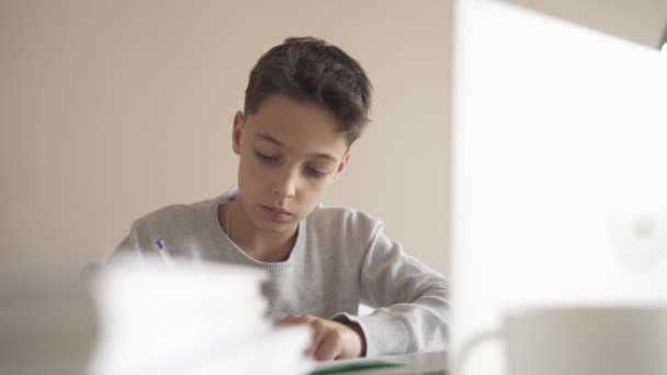 Een kind doet huiswerk met een laptop terwijl hij thuis in de keuken aan tafel zit. Online-technologie. — Stockvideo