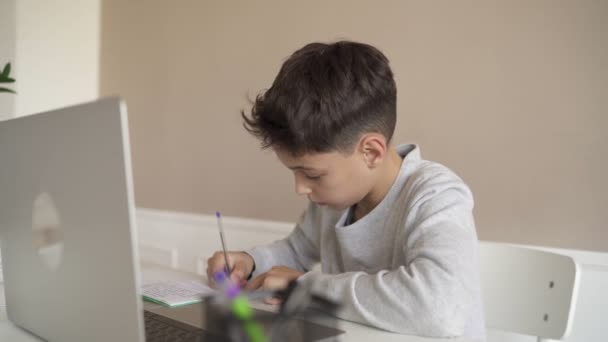 一个孩子坐在厨房的桌子边，一边用笔记本电脑做作业。在线技术. — 图库视频影像
