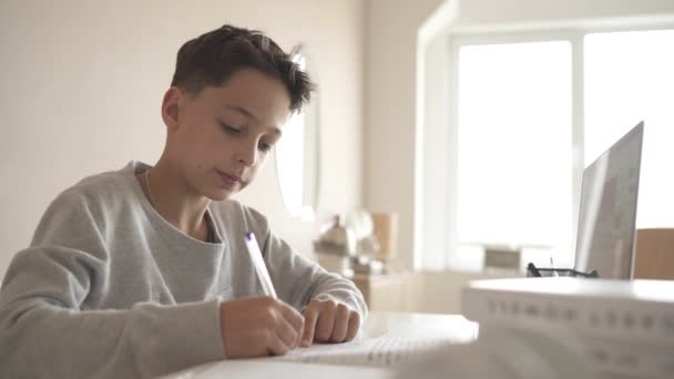 Een kind doet huiswerk met een laptop terwijl hij thuis in de keuken aan tafel zit. Online-technologie. — Stockvideo