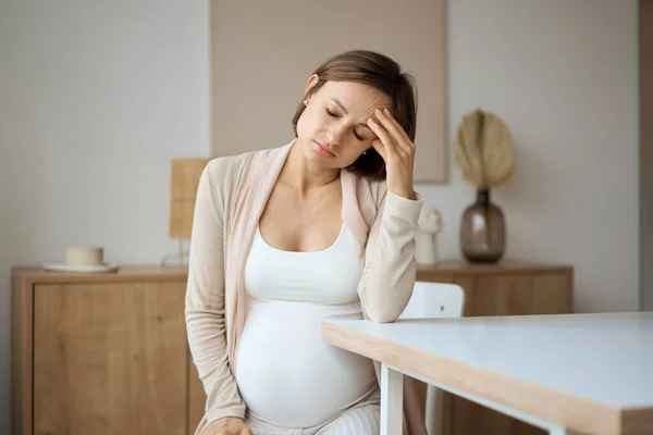 Wanita hamil menderita sakit kepala saat duduk di meja — Stok Foto