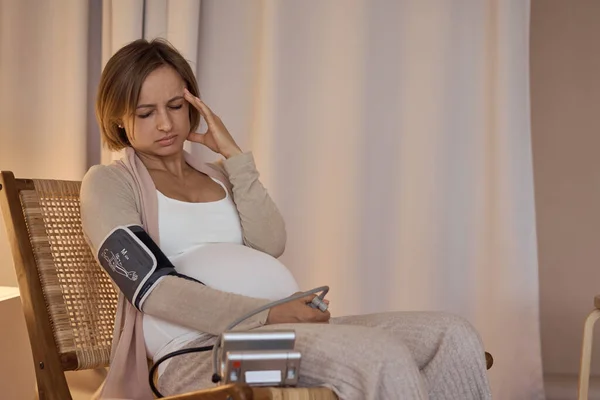 Wanita hamil mengukur tekanan darah dengan tonometer elektronik. neuralgia selama kehamilan, kesehatan yang buruk. Hipertensi. Kehamilan parah. Sakit kepala, migrain. — Stok Foto