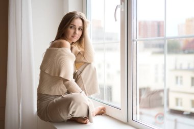 Düşünceli ve hayalperest bir kız pencerenin kenarında oturmuş elinde bir fincan aromatik kahve tutarken meşgul bir şehirde pencereden dışarı bakıyor.