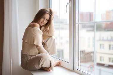 Düşünceli ve hayalperest bir kız pencerenin kenarında oturmuş elinde bir fincan aromatik kahve tutarken meşgul bir şehirde pencereden dışarı bakıyor.