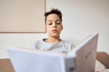 Beyaz çocuk evde kitap okuyor.