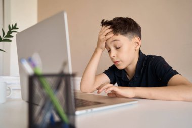 Akıllı çocuk ödevini yapıyor ve Covid-19 salgını ve sosyal mesafesi yüzünden evdeki bilgisayar defterine bakıyor..