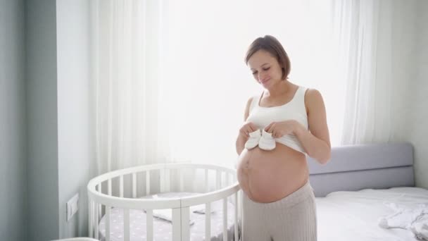 Молодая беременная женщина в маленьких кроссовках сидит дома на диване. Беременная мать готовится к родам. — стоковое видео