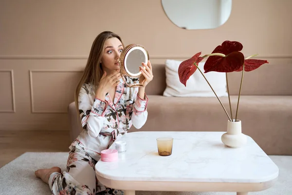 Belle femme en pyjama appliquant de la crème pour le visage. Jolie jeune femme en pyjama appliquant de la crème hydratante sur le visage. Frais du matin — Photo