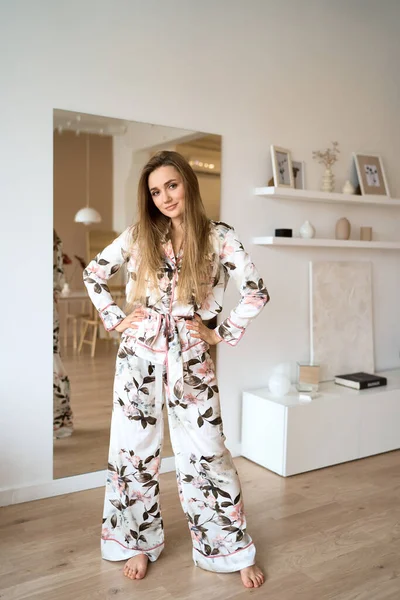 Trevlig morgon. Attraktiv ung kvinna i sidenpyjamas dansar nära spegeln i sin lägenhet. — Stockfoto